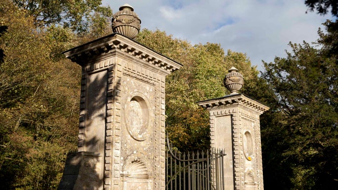 A pair of ornately decorated stone gateposts topped with a pair of stone urns at Coleshill Park in Oxfordshire